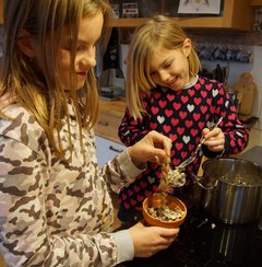 Zwei Kinder füllen Körnermasse in einen Tontopf