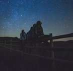 Mädchen sitzen auf Holzzaun und schauen Sternenhimmel an