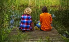 Zwei Kinder von hinten, die auf einer Holzbrücke sitzen