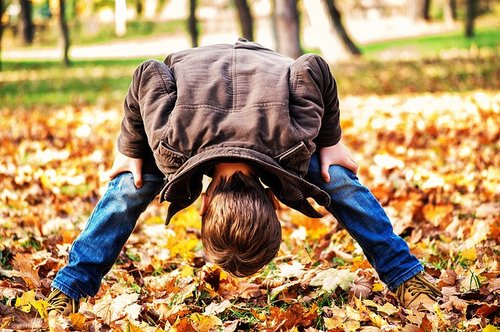 Ein Junge steht zwischen Herbstblättern und schaut durch seine Beine 